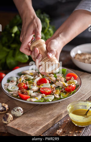 Leckere natürliche Salat mit fresly abgeholt grünes Gemüse, Hähnchen Fleisch und womans Hände Salz auf ein Brett. Stockfoto