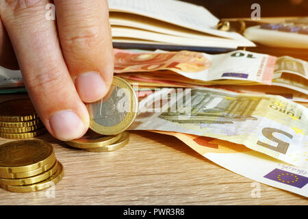 Der Mensch ist mit Euro-Münzen und -Banknoten auf einem Schreibtisch. Einsparungen. Stockfoto