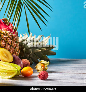 Verschiedene saftige exotische Früchte - Lychee, Ananas, Karambolen, Litschi, Dragon Obst auf einem grauen Holztisch auf einem blauen. Essen exotische Layout. Stockfoto