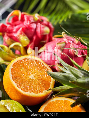 In der Nähe des exotischen Hintergrund aus frischen reifen tropischen Früchten dragon Früchte, Pitahaya, die Hälfte von Orange, Ananas Blatt. Stockfoto