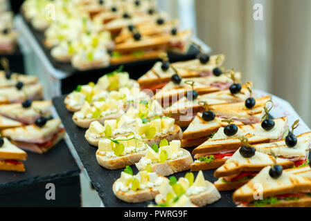 Häppchen mit Käse und Trauben und Sandwiches mit Speck und Kohl und Tomaten und Oliven auf einen Spieß auf einem Buffet Tisch Stockfoto