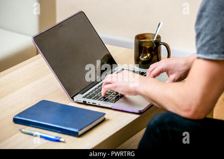 Junger Mann mit Brille, der an einem Notebook arbeitet in einem Home Office konzentriert. Sie auf einer Tastatur und scrollt Text auf dem Display. Seitenansicht