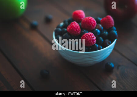 Schüssel mit Heidelbeeren und Himbeeren auf einem braunen Tisch. Stockfoto