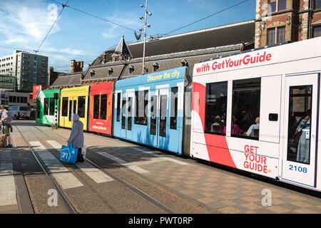 Amsterdam, Niederlande, Juli 23th, 2018: eine Straßenbahn am Hauptbahnhof von Amsterdam und eine Frau Tragetaschen ist dem Bahnübergang. Stockfoto