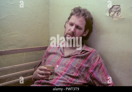 Ein Mann erscheinen unter dem Einfluss von Alkohol zu sein und das Leben im Slum-ähnlichen Bedingungen sitzt in einem depressiven Zustand gebeugt. Stockfoto