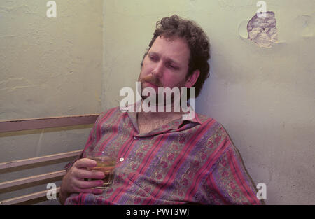 Ein Mann erscheinen unter dem Einfluss von Alkohol zu sein und das Leben im Slum-ähnlichen Bedingungen sitzt in einem depressiven Zustand gebeugt. Stockfoto