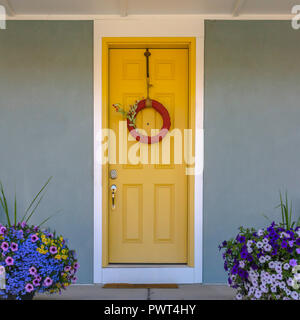 Vordere Tür mit Lorbeerkranz und bunten Blumen Topfpflanzen Stockfoto