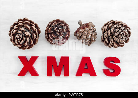 Thema Weihnachten. Pine Tree Kegel und das Wort Weihnachten in roten Buchstaben geschrieben, auf weißem Holz- Hintergrund. Stockfoto