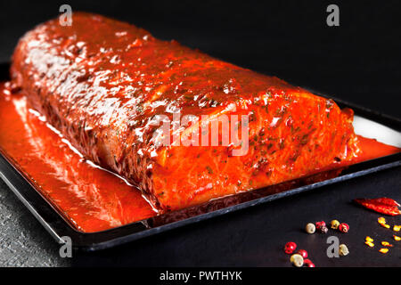 Ganze Stück mit mariniertem Schweinefilet bereit zu Kochen. Lende steaks Fach auf schwarzem Hintergrund mit Petersilie Stockfoto