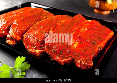 Filets Mariniertes Schweinefilet bereit zu Kochen. Lende steaks Fach auf schwarzem Hintergrund mit Petersilie Stockfoto