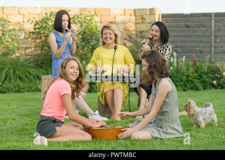 Die Familie Spaß, zwei Mütter mit Töchtern im Teenageralter singen und die Verwendung von Musikinstrumenten, Familie Musik Band, sitzen auf der Wiese in der Nähe der Th Stockfoto