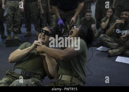 Lance Cpl. Stürmische Mendez, Links, und Lance Cpl. Amy Phan fühlen Sie den Ruck als 50-tausend Volt Kurs durch ihre Körper während nichttödliche Waffen Training an Bord der USS BONHOMME RICHARD (LHD 6), unterwegs in den Pazifischen Ozean, 20. Juni 2017. Mendez ist ein Grafiker und Phan ist ein Kampf Fotograf, beide mit 31 Marine Expeditionary Unit. Nichttödliche Waffen Ausbilder mit der Bekämpfung des logistischen Bataillon 31 Military Police Platoon ausgebildete Marinesoldaten und Matrosen aus dem gesamten 31. MEU setzen Taser und anderen tödlichen Waffen während Security Operations. Eine kritische Komponente der tödlichen Weap Stockfoto