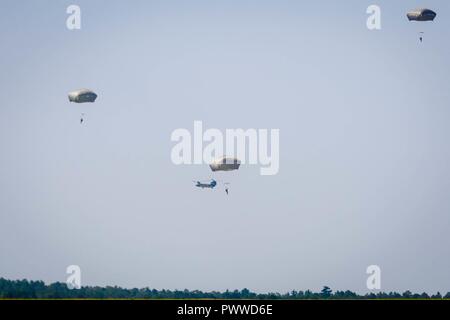 Eine CH-47 Chinook Hubschrauber 3. Allgemeine Unterstützung Aviation Battalion, 82nd Combat Aviation Brigade Kreise der Drop Zone als mehrere Soldaten mit 2Nd Battalion, 505Th Parachute Regiment, 3. Brigade Combat Team steigen während der luftgestützten Hilfsaktionen auf Sizilien Drop Zone in Fort Bragg, N.C., Juli 6, 2017. Stockfoto