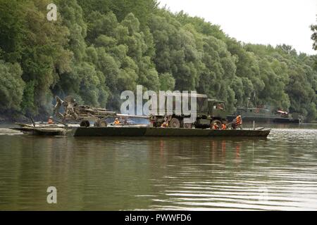 Soldaten zu Field Artillery Squadron, 2d-Cavalry Regiment, US-Armee zugewiesen haben ihre Light Medium Tactical Vehicle und M777 Haubitze über den Mosoni-Duna Fluss in Györ, Ungarn durch eine PMP schwimmende Brücke während der Übung Szentes Ax 17. Juli 4, 2017 transportiert. Die Brücke, die durch die Ingenieure von 37Th Engineer Regiment betrieben wird, Ungarische Verteidigung und Feuerwehr 837th Engineer Battalion, U.S. Army National Guard von Wooster, Ohio. Die Ungarische Nationale Bewegung findet statt am 26. Juni - 7. Juli Sabre Guardian 17 durch taktische Bridging und Wasser Kreuzung Operationen für 2CR frei zu aktivieren Stockfoto