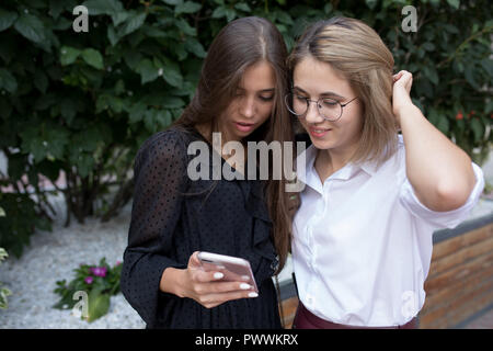 Zwei junge Frauen stehen auf der Straße und mit einem Smartphone. Stockfoto