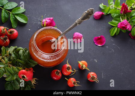 Hellen Grüns eines Hundes - rosenbusch mit Beeren und Blumen auf dem Tisch neben einem marmeladenglas. Stockfoto