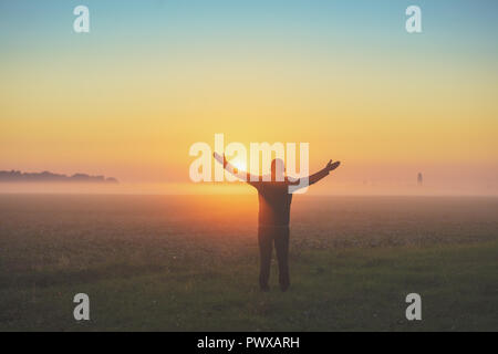 Glückliche Menschen mit den Händen in der Luft steht im Bereich des Morgens früh auf und genießen den Sonnenaufgang Stockfoto