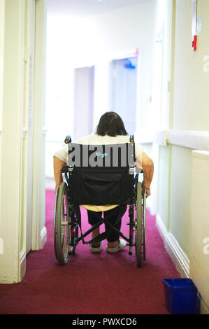 Die älteren behinderten Frau selbst in einem Rollstuhl mit einem Korridor in einer Regierung care Home drücken Stockfoto