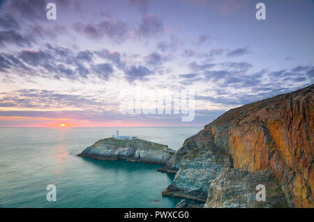 Abend Landschaft schoss der untergehenden Sonne am Horizont, mit Blick aufs Meer in Richtung South Stack Lighthouse, Anglesey, North Wales, UK. Wispy cirrus Cloud. Stockfoto