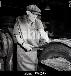 1950er Jahre, in eine Fabrik, eine männliche Arbeiter in Overalls und trägt ein flacher Deckel Runderneuerung von Reifen, England, UK. Reifen Runderneuerung oder Instandsetzung verlängert die Lebensdauer von einem abgenutzten Reifen durch die Hinzufügung eines neuen Lauffläche Gummi, also die Erweiterung und die Maximierung der Lebensdauer eines ursprünglichen Reifen und Einsparung von Ressourcen verwendet, Reifen wie Öl zu machen. Stockfoto