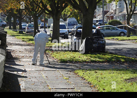 Liverpool, Großbritannien. 18. Oktober 2018. Eine Polizeikette um eine ausgebrannte Autos in Abbeystead Straße Childwall. Einen dunklen Audi verlassen auf einem Gras Kante, 1,7 Meilen von der Aufnahme der letzten Nacht in Alderson Rd, Wavertree. Ein forensics officer Fotos und sammeln Beweise am Tatort. Die Polizei nicht sagen, zu diesem Zeitpunkt, wenn das Auto in der vergangenen Nacht Mord beteiligt war. Credit: Ken Biggs/Alamy Leben Nachrichten. Stockfoto