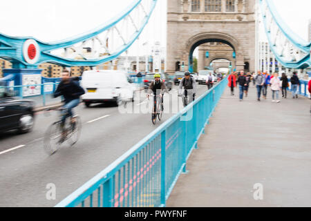 London, Großbritannien. Ein Radfahrer trägt einen hellen gelben Helm Pedale Vergangenheit im hektischen Berufsverkehr über die Tower Bridge. Stockfoto