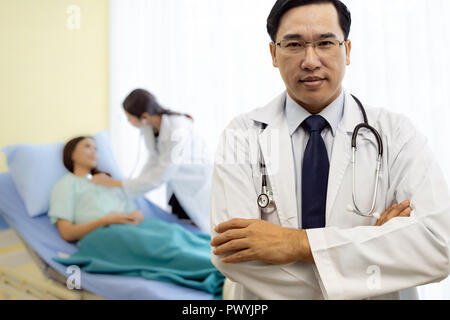 Portrait von jungen Erwachsenen Arzt mit Krankenschwester und Patient im Hintergrund. Stockfoto
