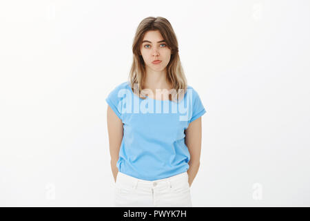 Portrait von unglücklichen Weiblich Mitarbeiter in blauen T-Shirt, schmollen und Schmollen, an der Kamera den Blick mit Mangel an Interesse, gleichgültig und unbeeindruckt, stehend Umkippen über grauer Hintergrund Stockfoto