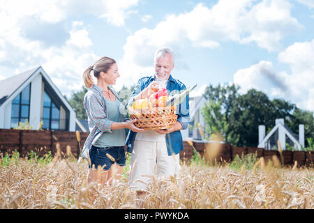 Glückliches Paar sammeln Ihre schöne Ernte und setzen es in großen Korb Stockfoto