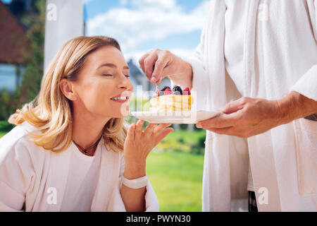 Fürsorglichen Mann tragen weiße Bademantel leckere Pfannkuchen, seine attraktive Frau Stockfoto