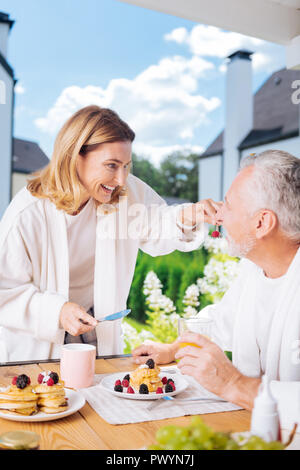 Liebevolle strahlendes Paar tragen weiße Bademäntel Frühstück außerhalb Stockfoto