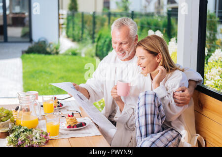 Strahlendes paar News lesen Nach dem Frühstück und trinken Orangensaft Stockfoto