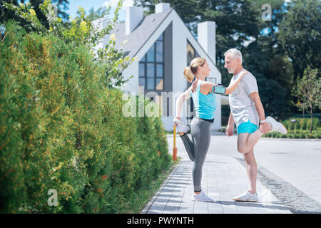 Schöne schlanke Frau lehnte sich auf ihren Ehemann während Stretching nach dem Ausführen Stockfoto