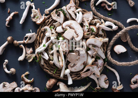 Hohe Betrachtungswinkel von einem Stapel von Raw gemischte Pilze, wie z. B. gemeinsame Champignons, Austernpilze und Shiitake, auf einem grauen rustikalen Holztisch Stockfoto