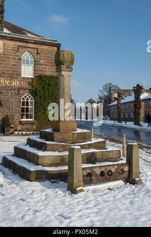 Snowy Winter Blick auf die Boars Head Hotel in Ripley in North Yorkshire, mit dem Kreuz und der Bestände vor dem Hotel Stockfoto