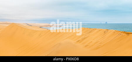 Lange gelbe Sanddüne von Kalahari Wüste und Atlantik Ufer, mit Bohrinseln und Schiffen am Horizont, in der Nähe von Swakopmund, Namibia Stockfoto