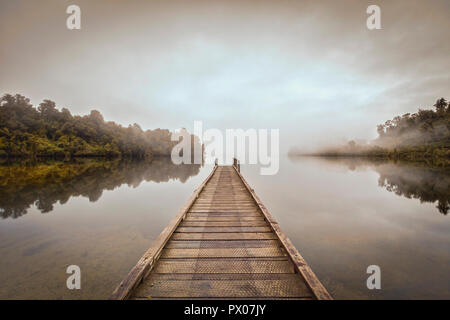 Ein Steg auf einem ruhigen See Mapourika, Neuseeland, mit Nebel driften über in der Morgendämmerung. Stockfoto