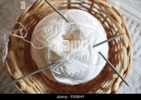 Kugel aus weißer Wolle und Stricknadeln in einem Weidenkorb. Retro und Vintage Aktivitäten Konzept Stockfoto