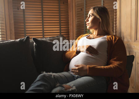 Schwangere Frau sitzt auf einem Sofa auf der Suche durch das Fenster Stockfoto