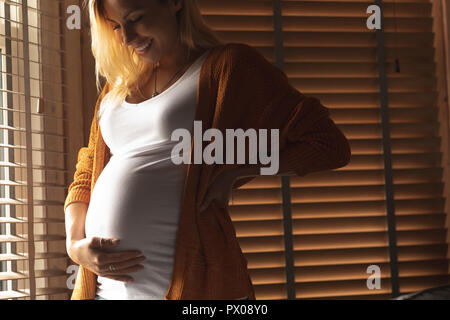 Schwangere Frau ihren Bauch berühren, in der Nähe der Fenster Stockfoto