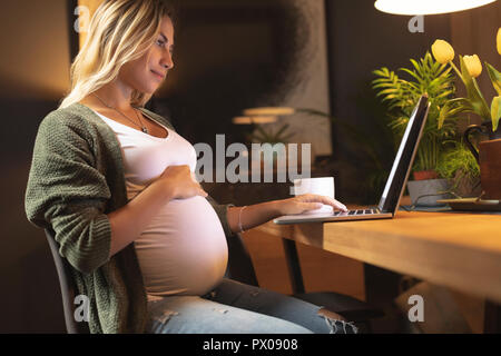 Schwangere Frau ihren Bauch und mit Laptop berühren Stockfoto