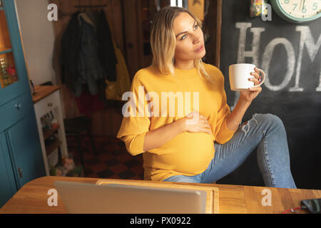 Schwangere Frau mit Kaffee Tasse schauen aus dem Fenster Stockfoto