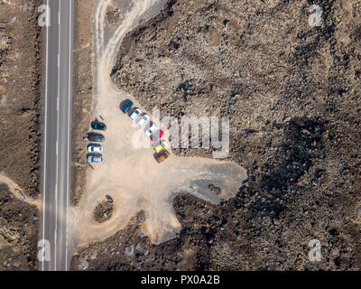 Luftaufnahme von einer Straße, die durch Lavafelder und Autos zwischen der gegliederten Küste von Lanzarote, Kanarische Inseln, Spanien, Afrika geparkt. Stockfoto