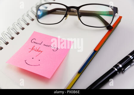 Guten Morgen, Freitag, auf einem Post-it auf einem Notizblock mit Brille nach oben geklebt geschrieben. Stockfoto