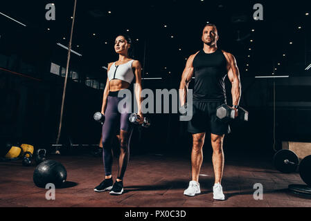 Fit Sportler und Sportlerin mit Hanteln zusammen trainieren in dunklen Fitnessraum Stockfoto