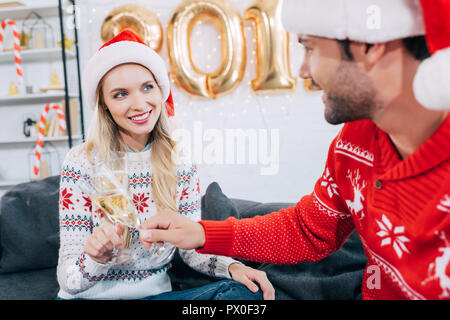 Lächelnd Ehepaar in Santa Hüte Toasten mit Champagner Gläser und feiern das neue Jahr zu Hause Stockfoto