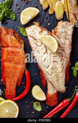 Filet von der Heiß geräucherten Red Snapper auf einem schwarzen Steinplatte mit Gewürzen, Kräutern und in Scheiben geschnittene Zitronen, vertikale Ansicht von oben, close-up Stockfoto