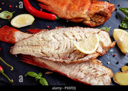 Filet von der Heiß geräucherten Red Snapper auf einem schwarzen Steinplatte mit Gewürzen, Kräutern und in Scheiben geschnittene Zitronen, Ansicht von oben, close-up Stockfoto