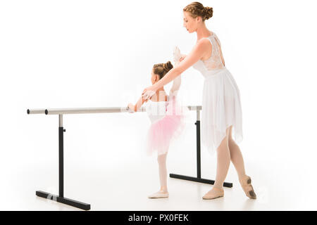 Seitenansicht der weiblichen Lehrer in Tutu helfen Kleine Ballerina üben an ballet Barre stand auf weißem Hintergrund Stockfoto