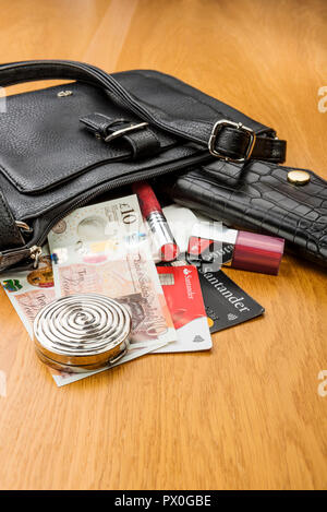 Damen Handtasche und Geldbörse, der Inhalt entleert. Zeigt einige Kosmetika, Bargeld und Kreditkarten. Stockfoto